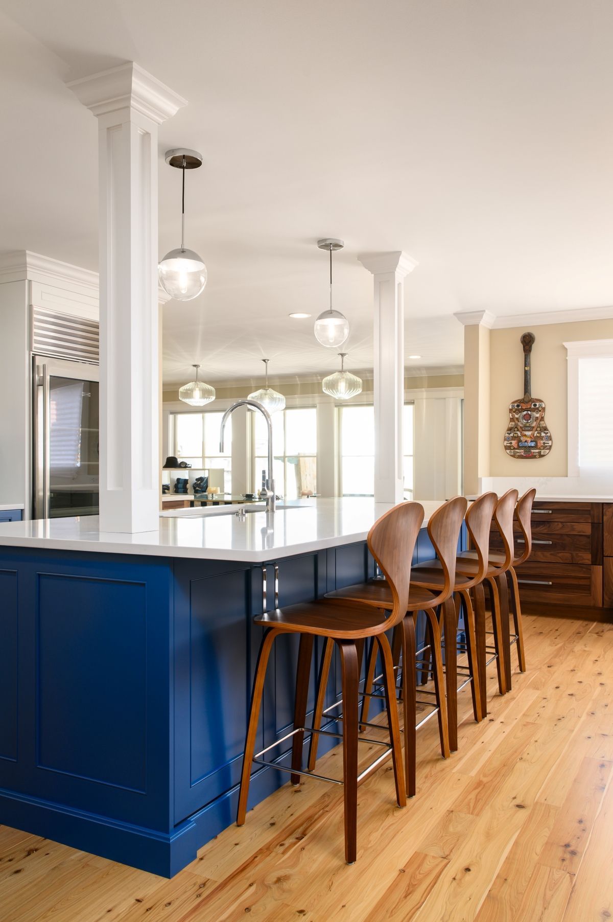 Bright kitchen with blue island, wooden stools, pendant lights, and hardwood floors