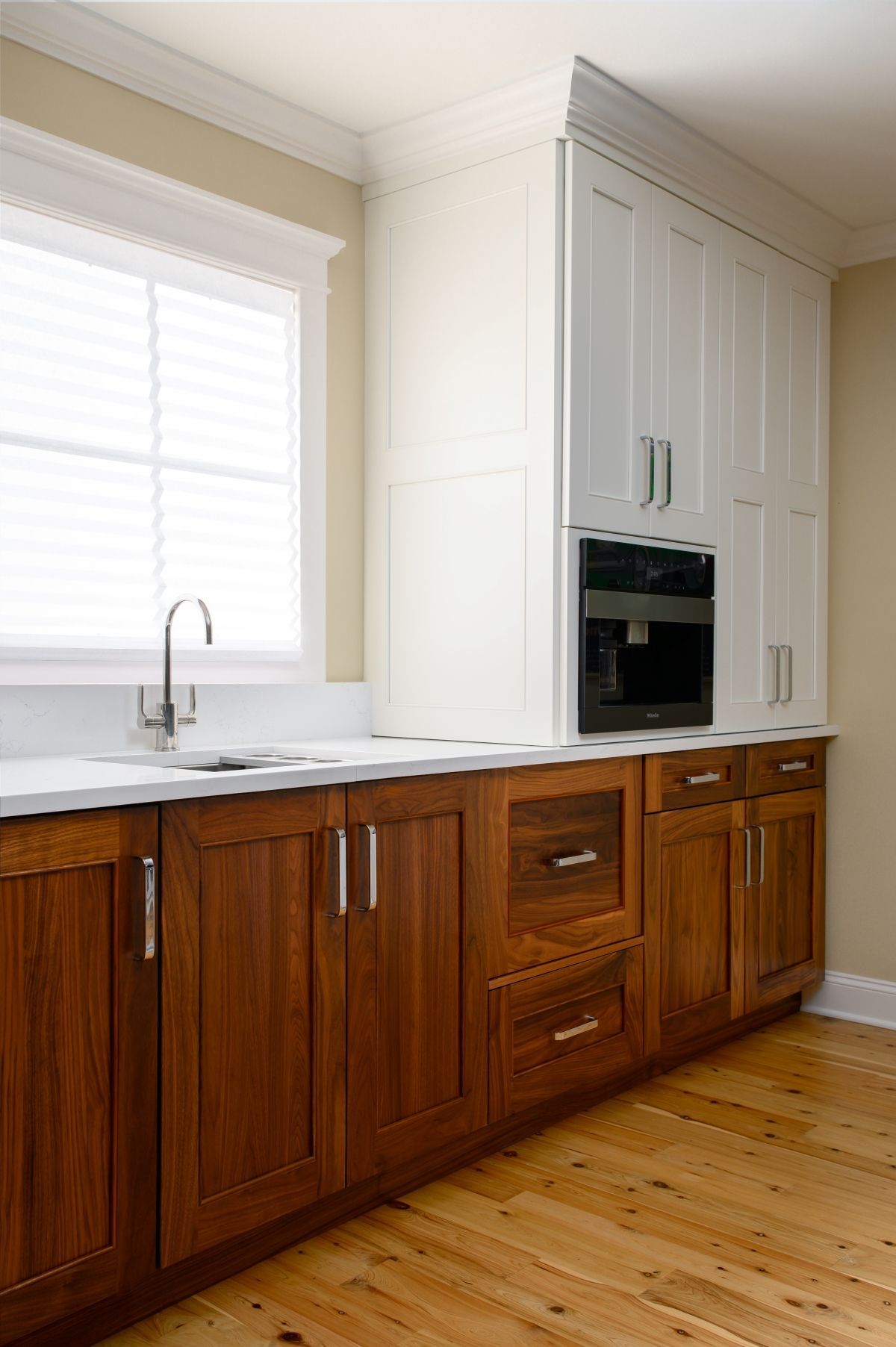 Modern kitchen with white upper cabinets, dark wood lower cabinets, and a large window over the sink.