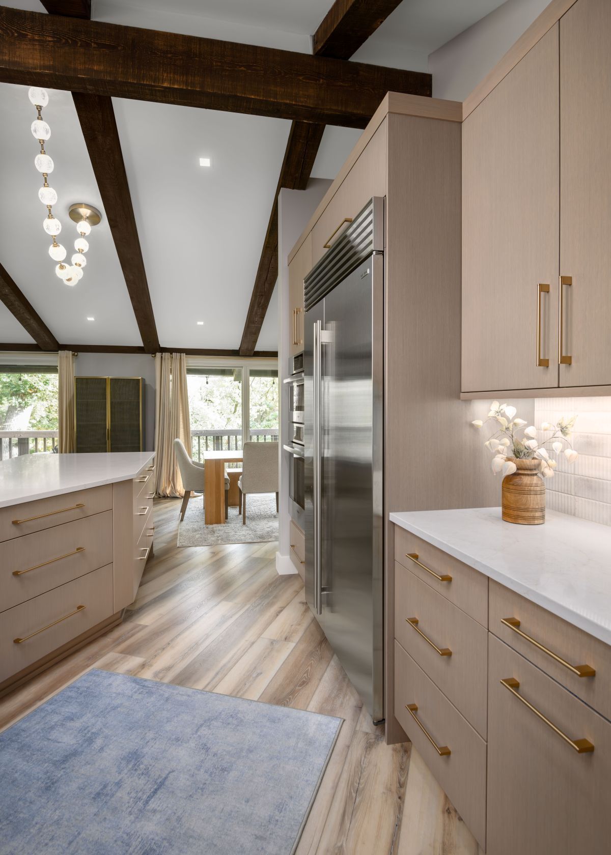 Modern kitchen with light wood cabinets, island, stainless appliances, and exposed beams near a dining area.