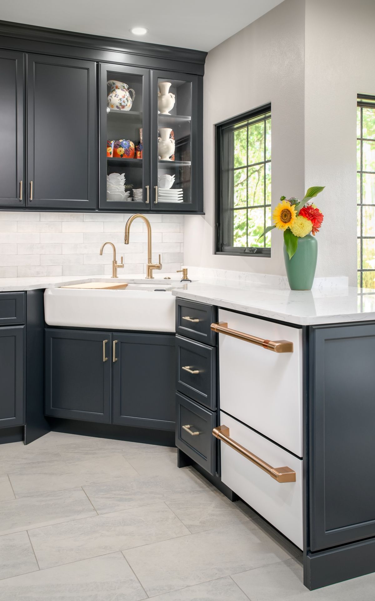 Modern kitchen with dark cabinets, white countertops, gold fixtures, and a vase of flowers by the window