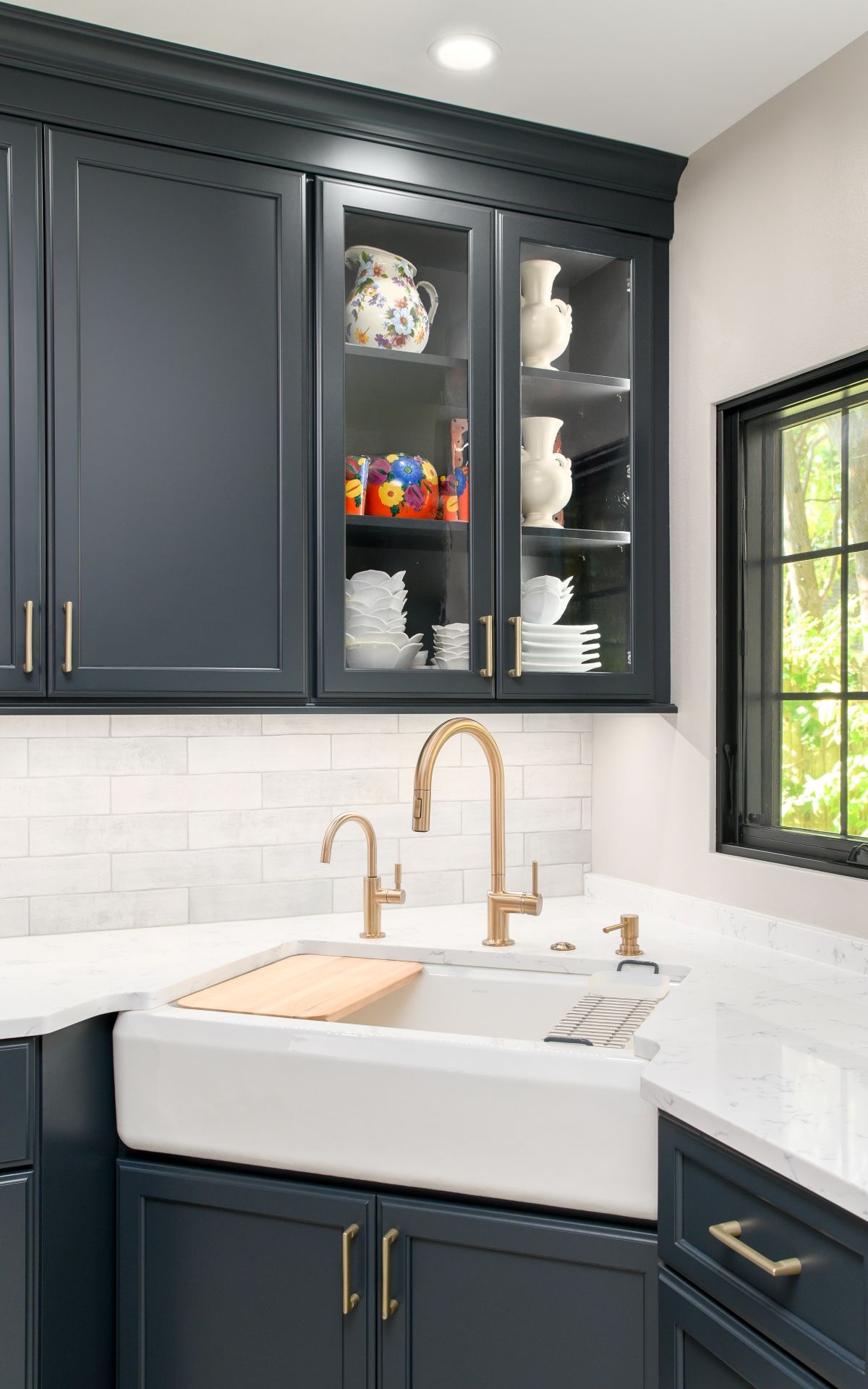 Modern kitchen with dark cabinets, white sink, brass faucet, and glass-front display cabinet.