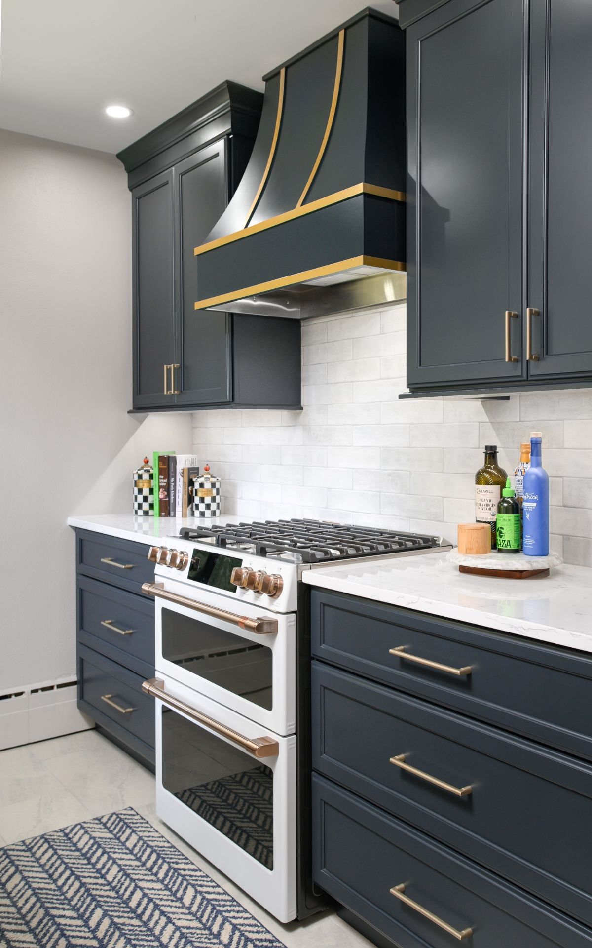 Modern kitchen with dark gray cabinets, white backsplash, stainless stove, and black range hood.