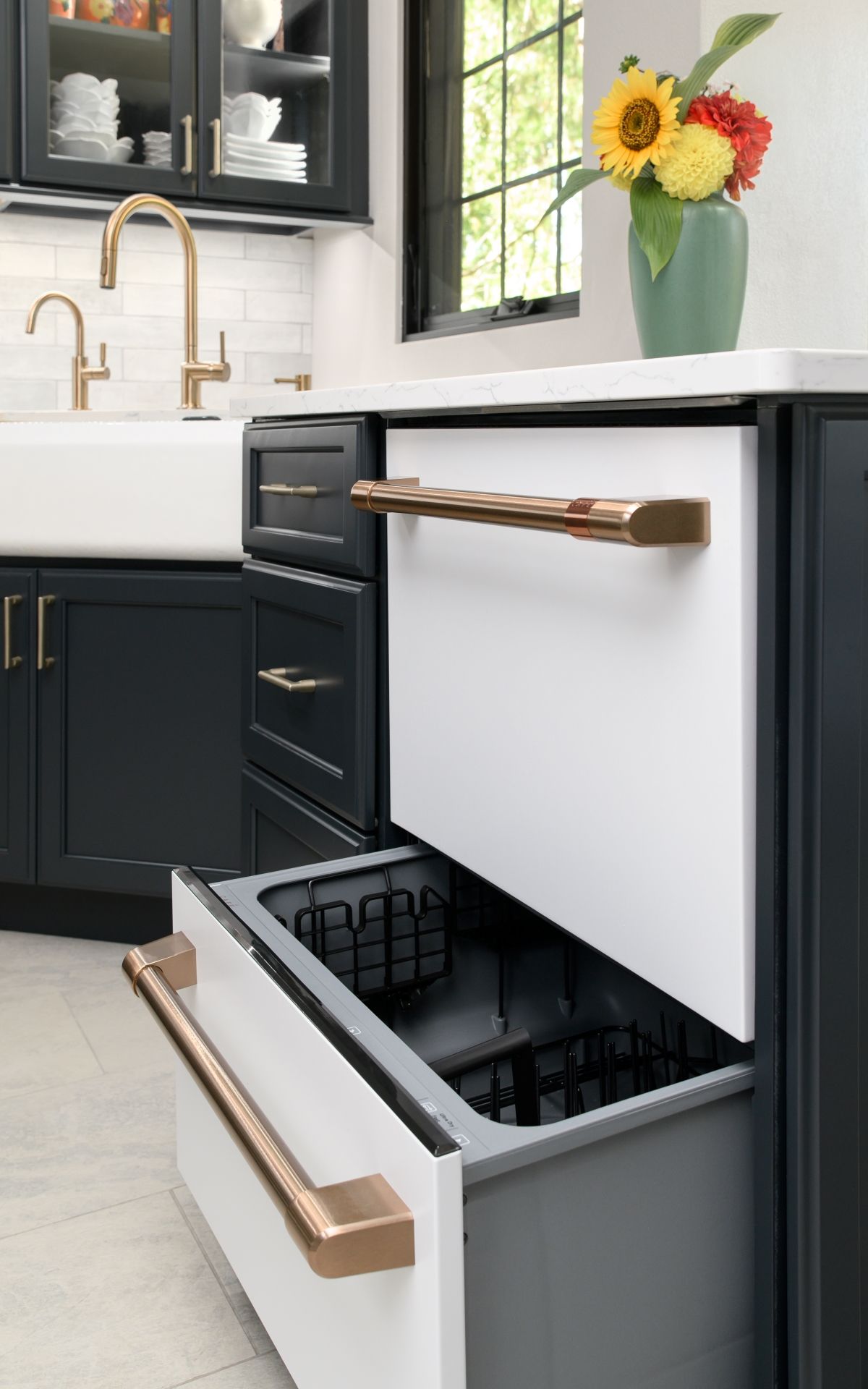 Modern kitchen with open drawer showing cutlery and drawers, white cabinets, dark lower cabinets, and flowers on the counter