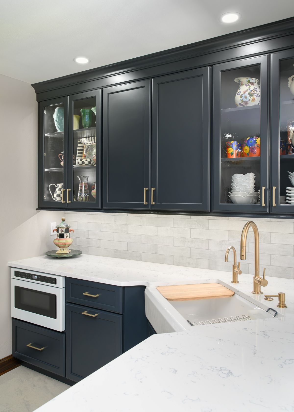 Modern kitchen with dark cabinets, glass-front shelves, white countertops, and gold faucet/sink fixtures