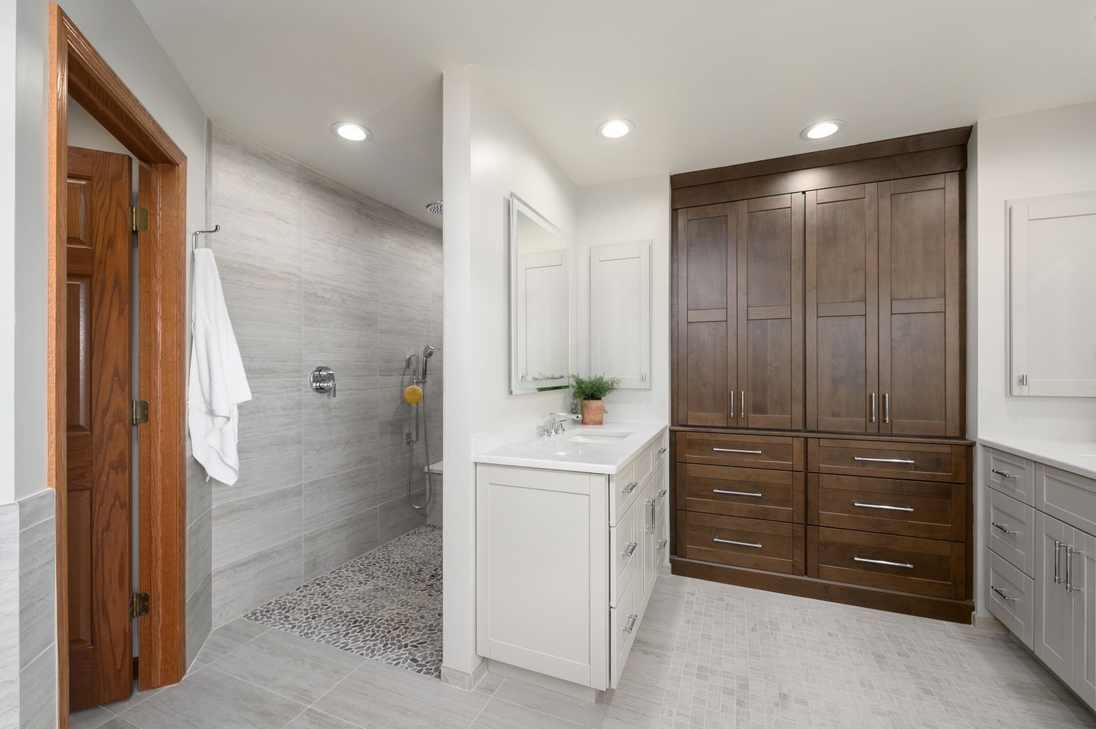 Bright bathroom with walk-in shower, white vanity, and large wooden storage cabinets.