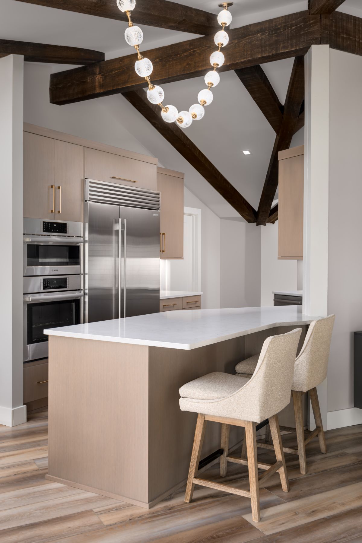 Modern kitchen with island, white countertops, stainless appliances, and exposed dark wood beams