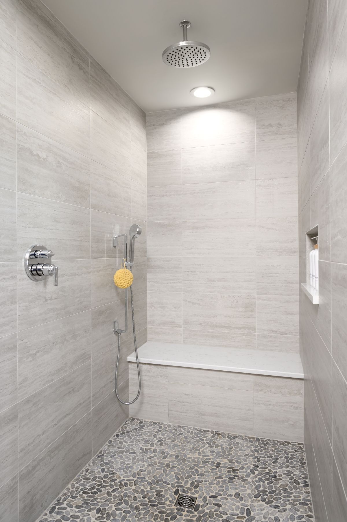 Tiled walk-in shower with rain showerhead, handheld sprayer, built-in bench, and pebble floor.