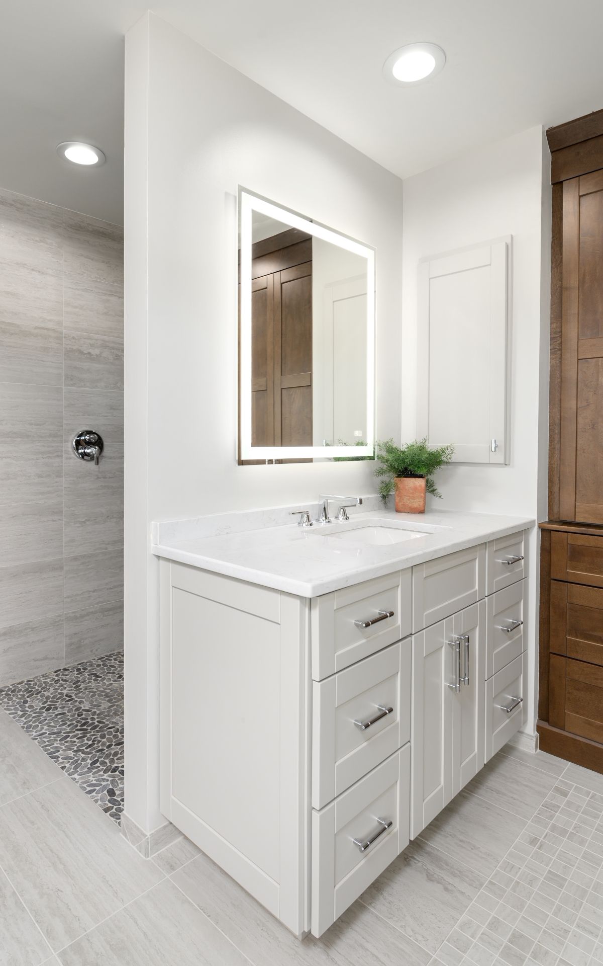 Modern white bathroom vanity with sink, mirror, and walk-in shower in a bright, clean room