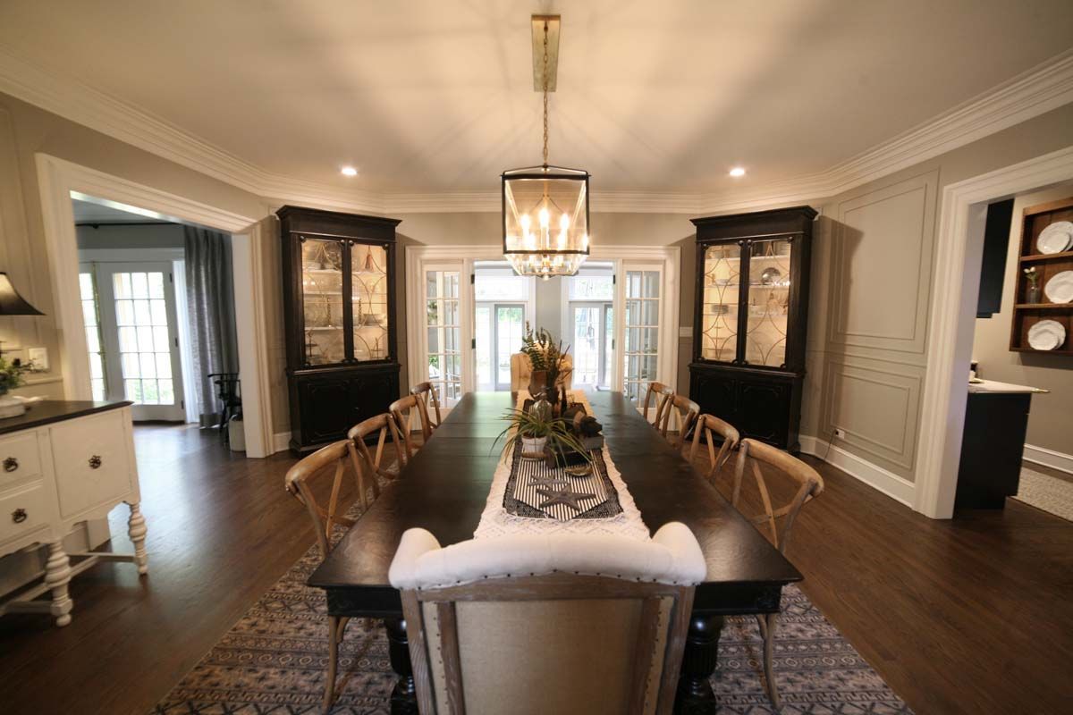 Elegant dining room with long table, chandeliers, dark wood cabinets, and French doors.