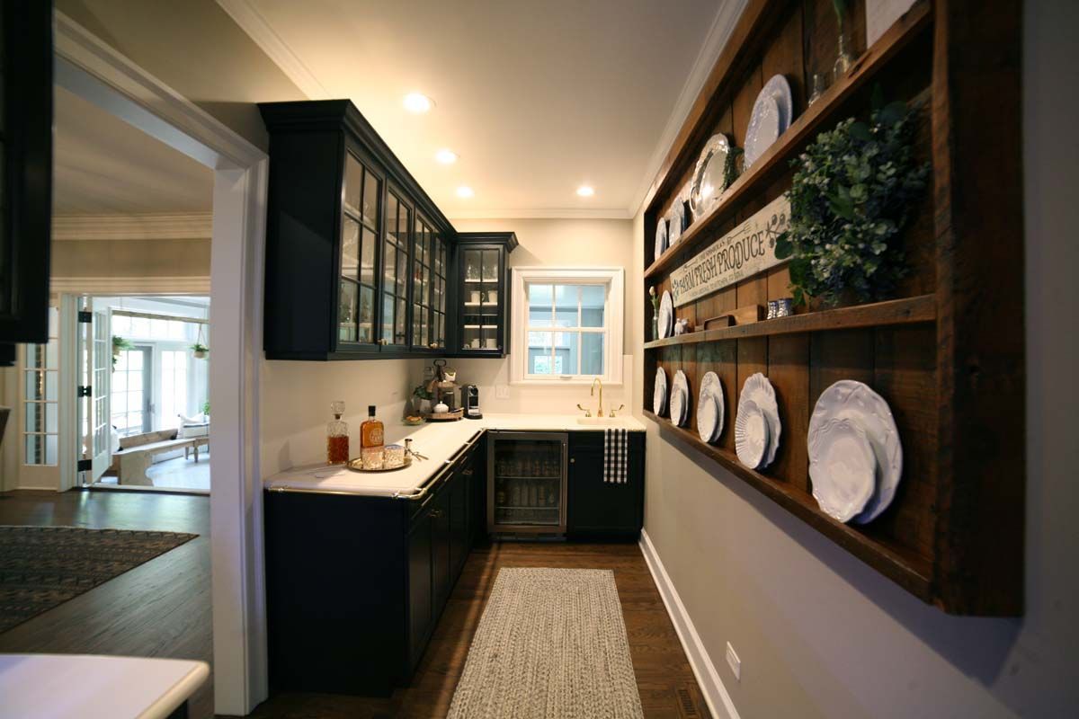 Narrow kitchen with dark cabinets, white countertops, and plate display shelves on the right wall.