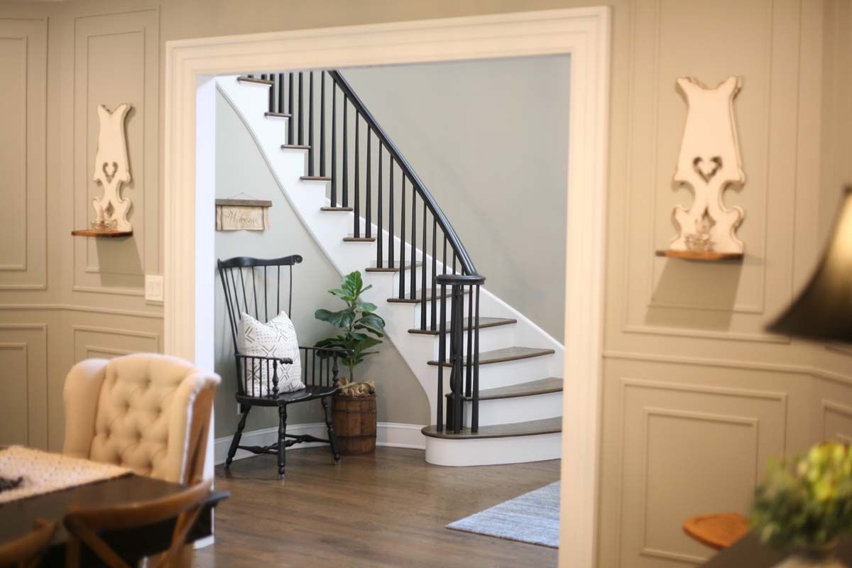 Elegant foyer view through a doorway to a staircase with black railings, white walls, and a chair by the hall