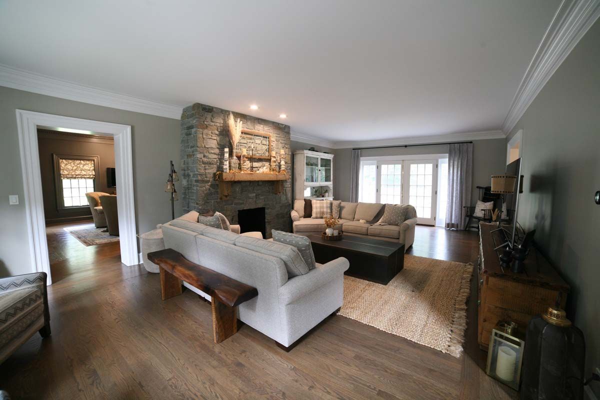 Bright living room with white sofas, stone fireplace, wood floors, and large windows.