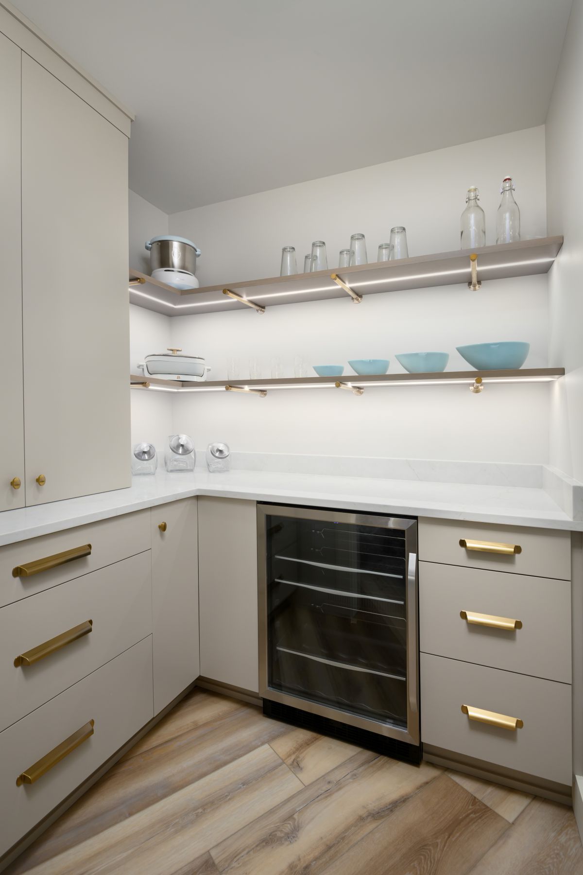 Modern kitchenette with white cabinets, brass handles, open shelves, and a wine fridge under a countertop