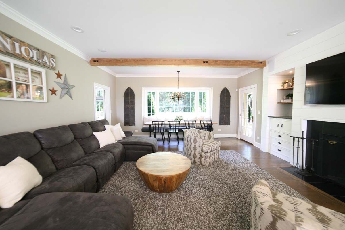 Bright living room with dark sectional sofa, shag rug, and TV on a wall beside a dining area.