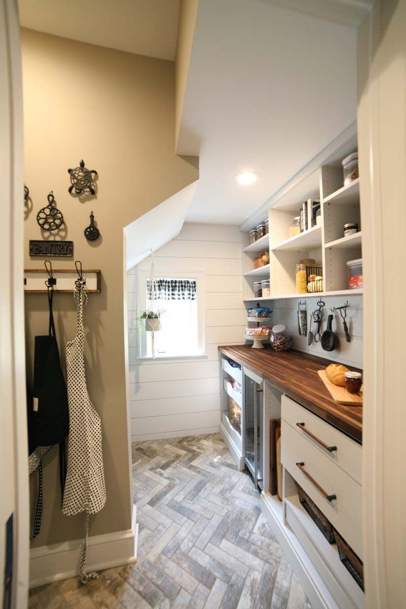 Narrow kitchen hallway with white cabinets, wood countertops, herringbone floor, and built-in shelves
