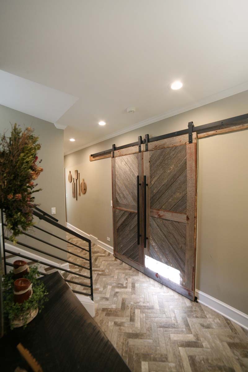 Modern interior hallway with barn doors, staircase railing, recessed lights, and herringbone wood floor
