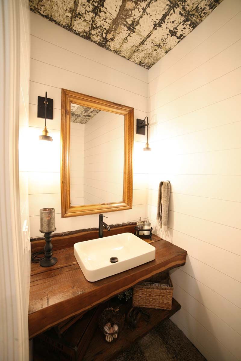 Small rustic bathroom vanity with a sink, gold-framed mirror, wall sconces, and wood countertop.