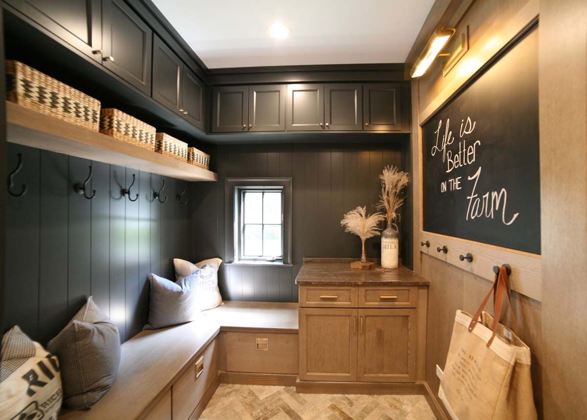 Narrow mudroom with dark cabinets, bench, hooks, chalkboard wall, and a small window seat.
