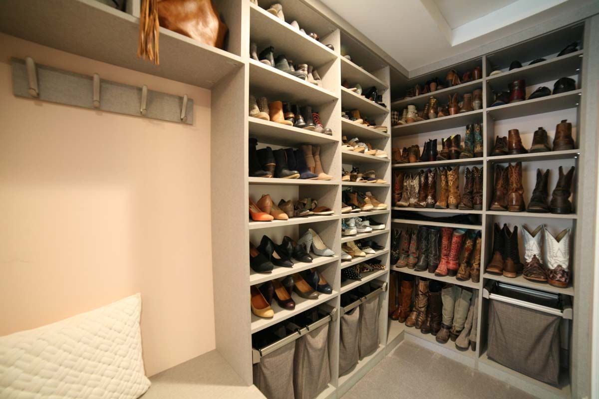 Walk-in closet with shelves and hanging racks filled with shoes and boots in a bright room