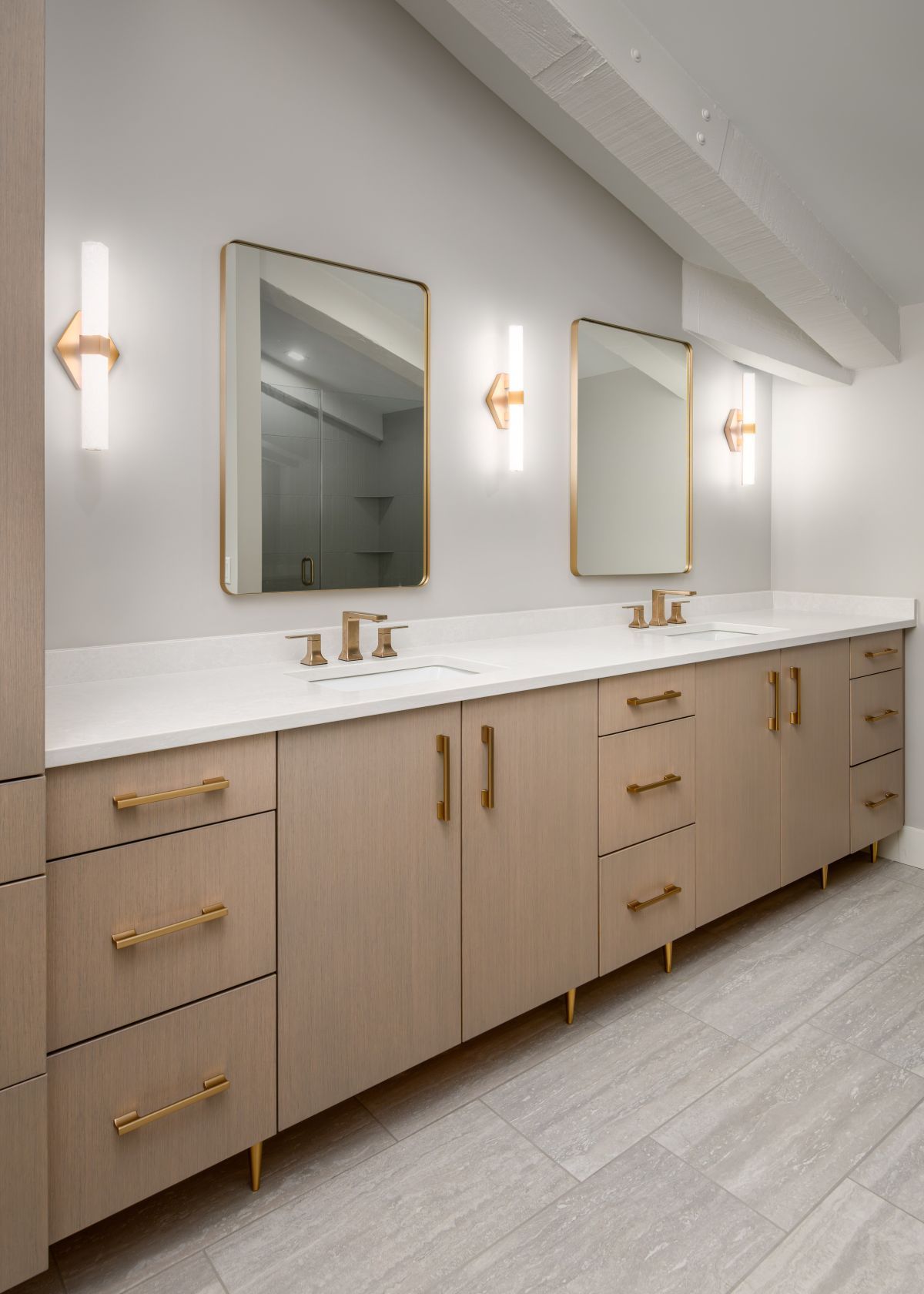 Modern double bathroom vanity with light wood cabinets, gold accents, and wall mirrors under sconces