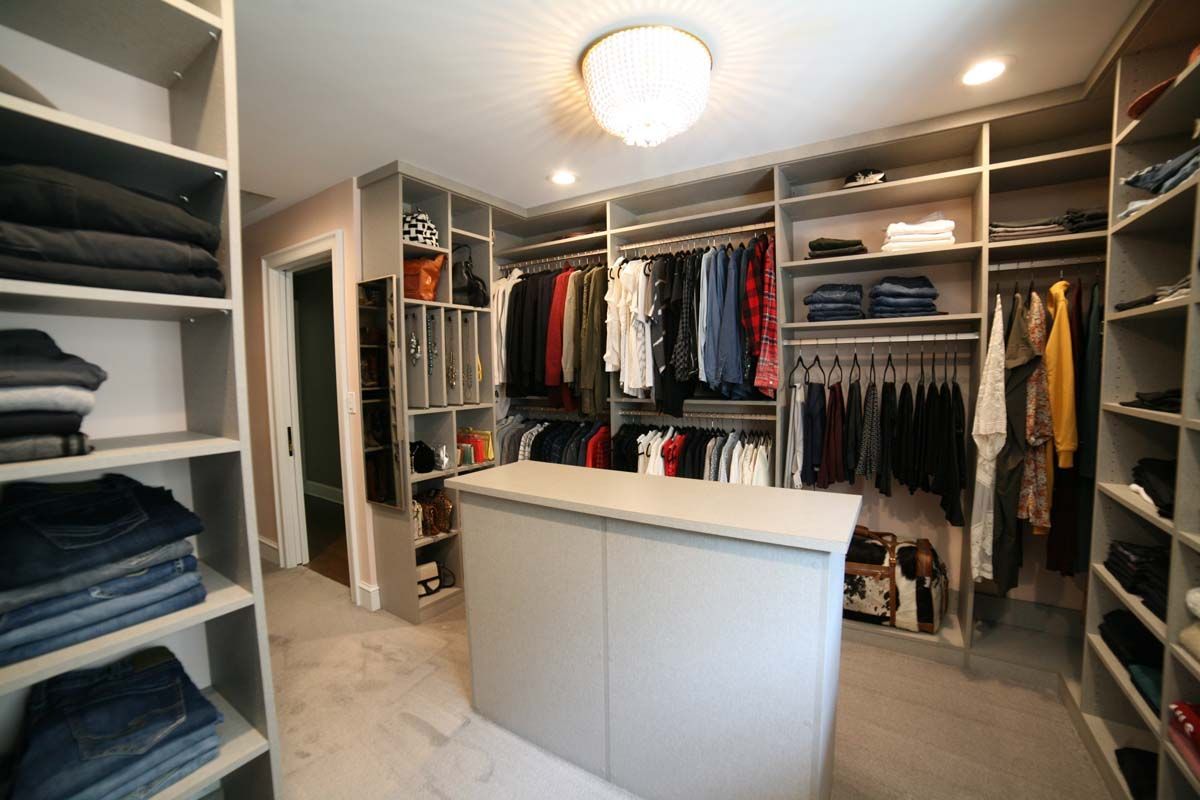 Walk-in closet with open shelving, hanging clothes, and a central white island under a ceiling light