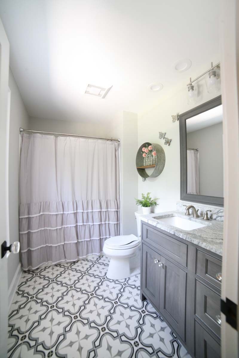 Bright bathroom with patterned tile floor, gray vanity, shower curtain, toilet, and wall mirror
