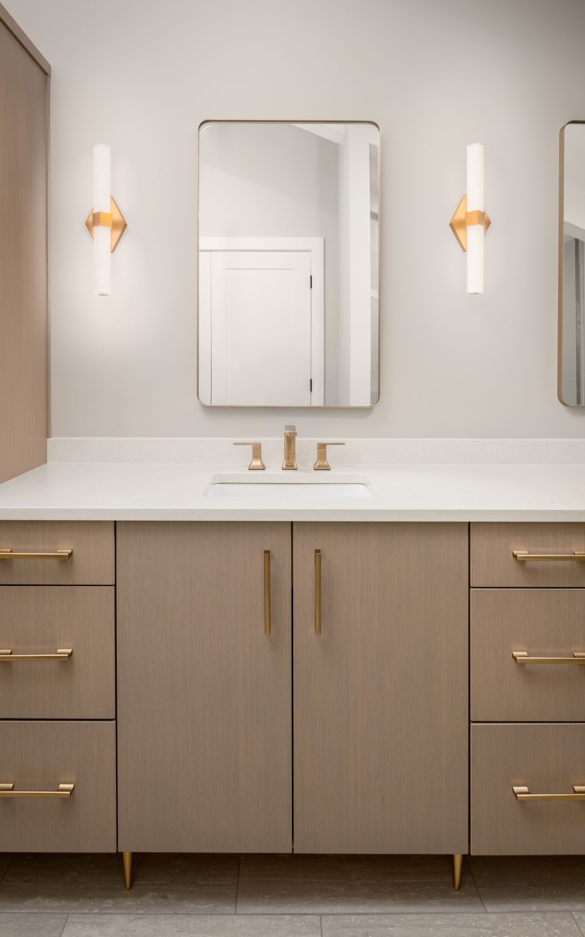 Modern bathroom vanity with double sinks, gold fixtures, wall sconces, and a centered mirror.