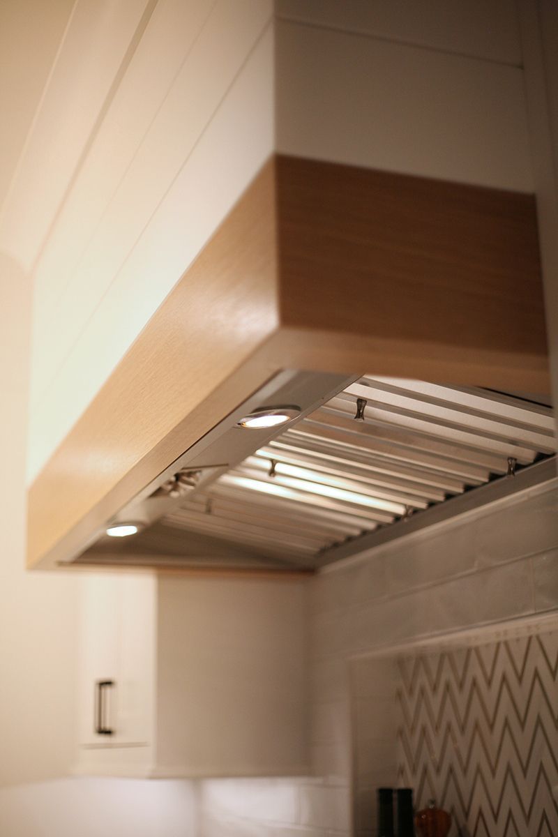 Modern kitchen range hood in white and wood tones above a stovetop