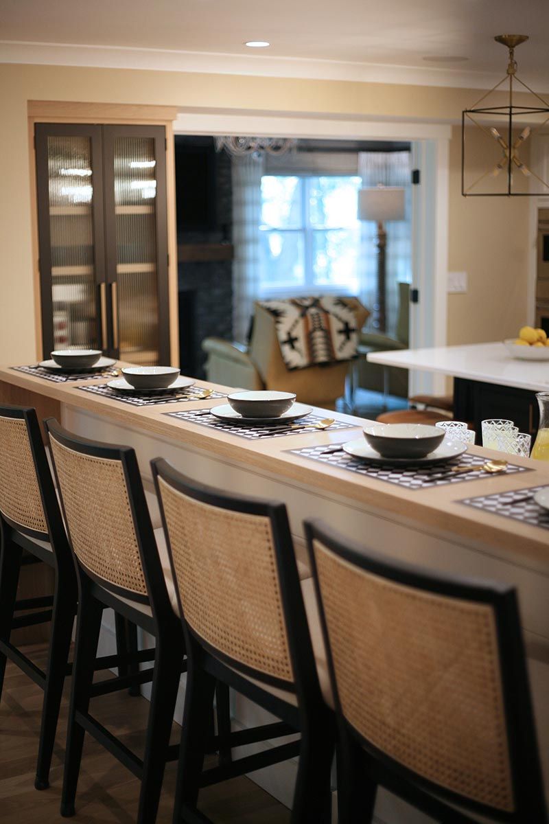 Dining room with a set table, bar stools, and a view into a bright adjoining room