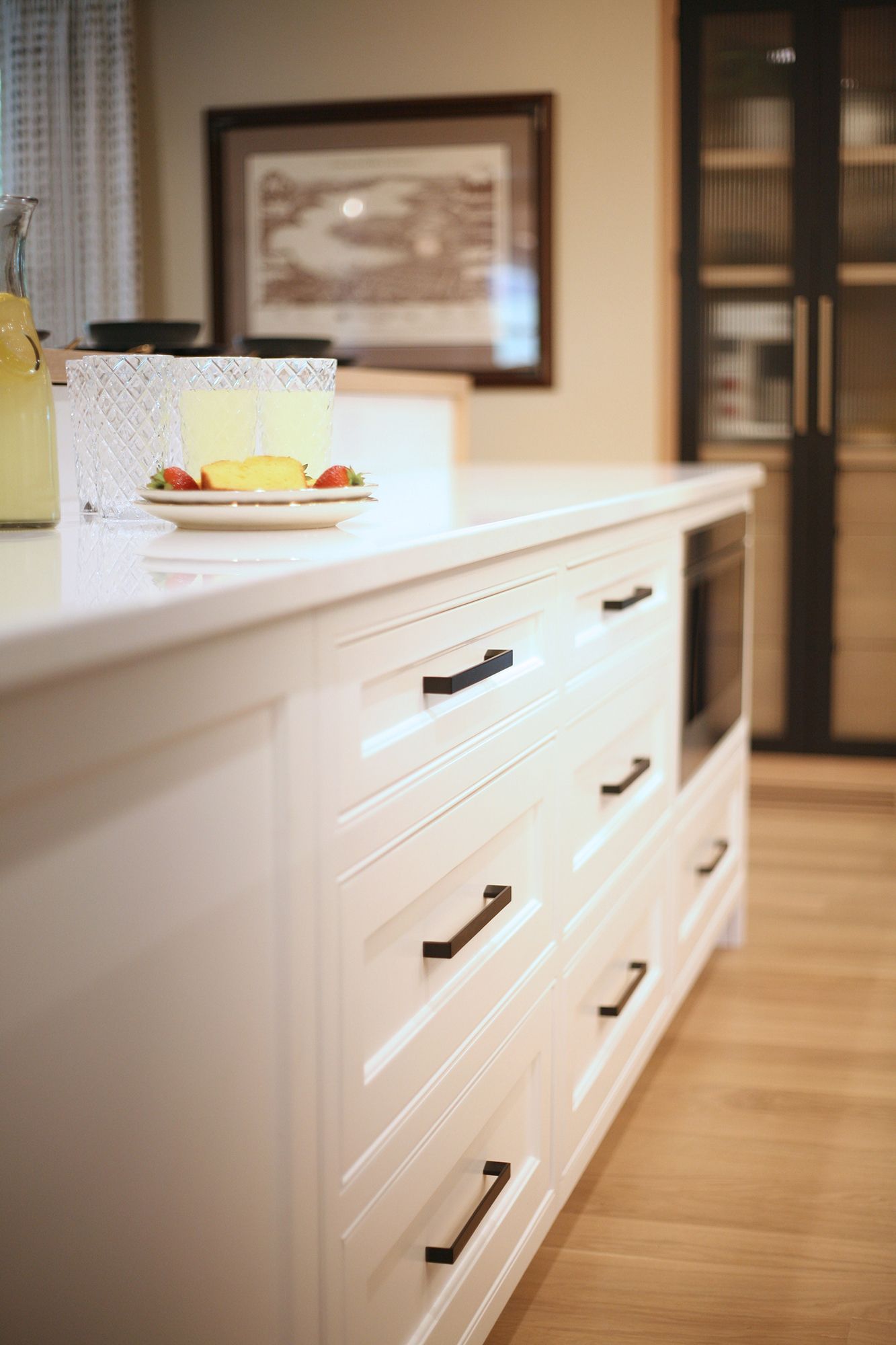 Kitchen island with white drawers, a plate of fruit, and warm wood flooring in a modern home