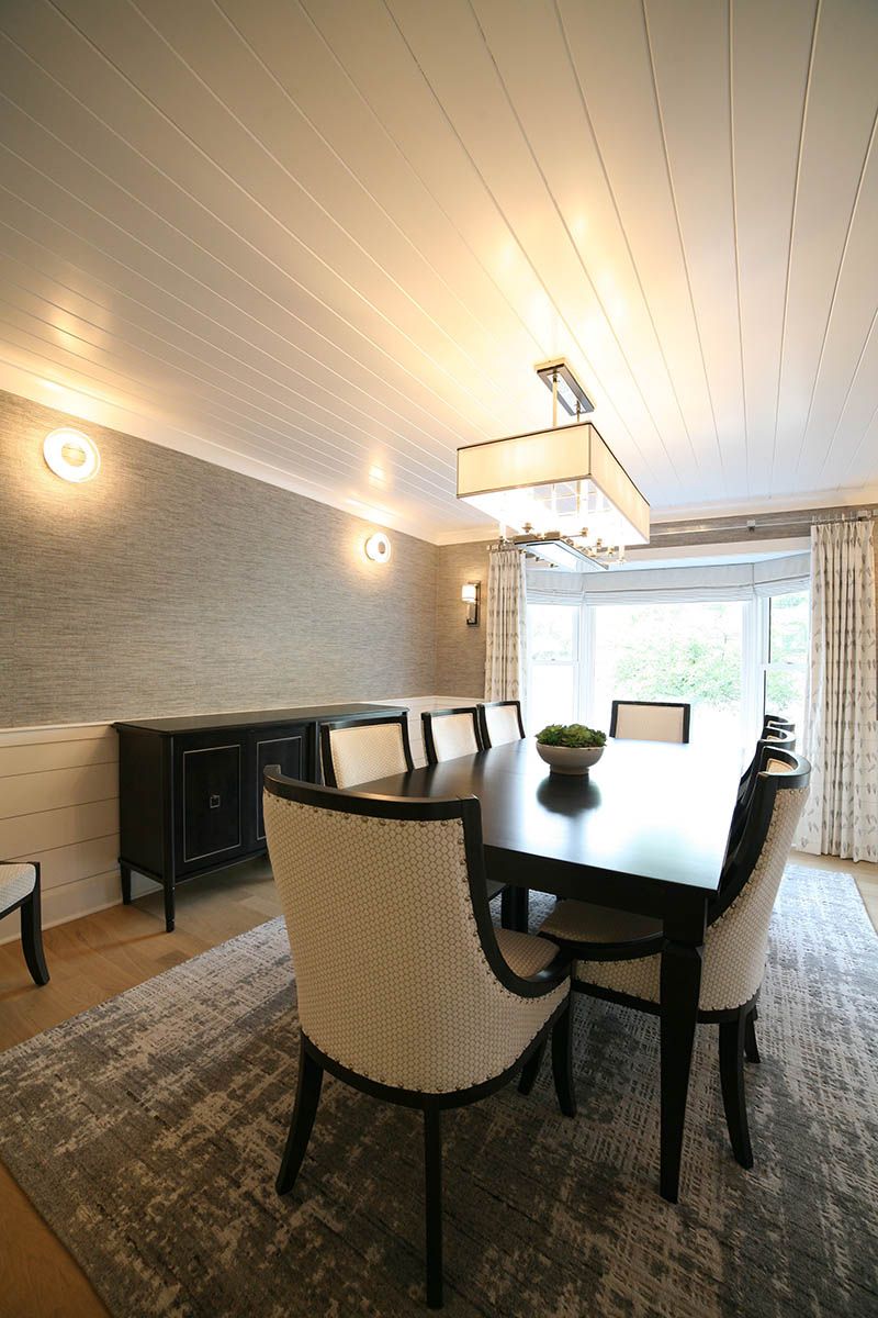Elegant dining room with a dark table, upholstered chairs, chandelier, and large window with sheer curtains.