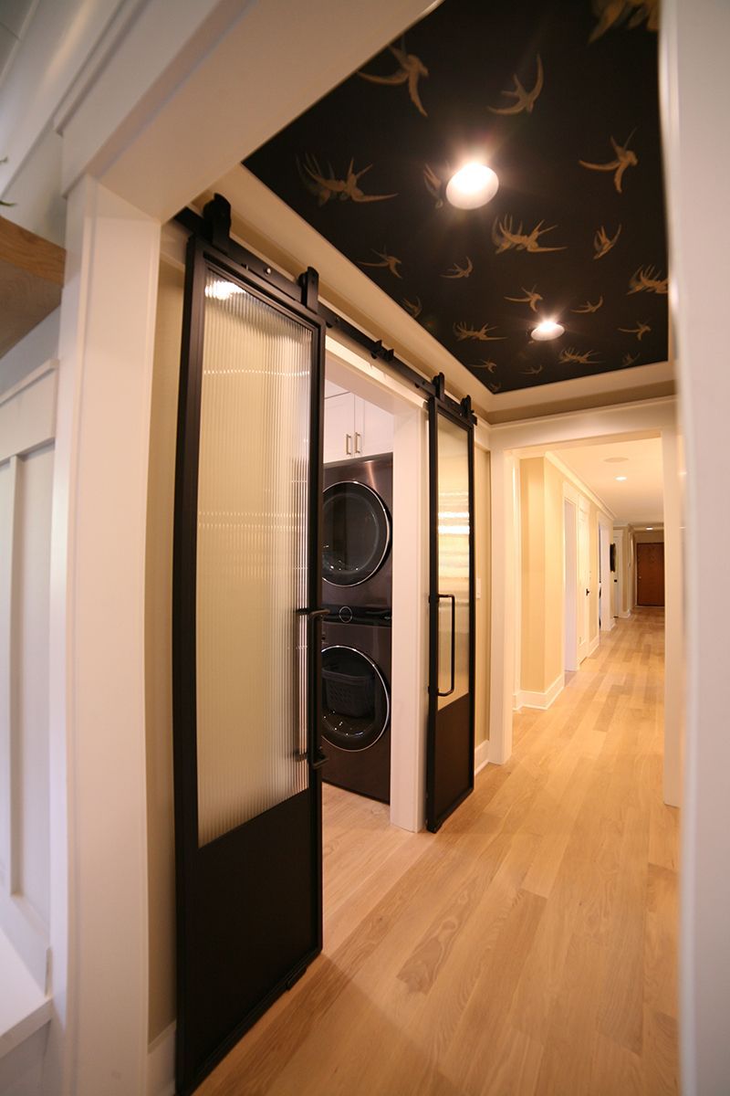 Modern hallway with light wood floors, dark ceiling with bird pattern, and black-framed doors on one side
