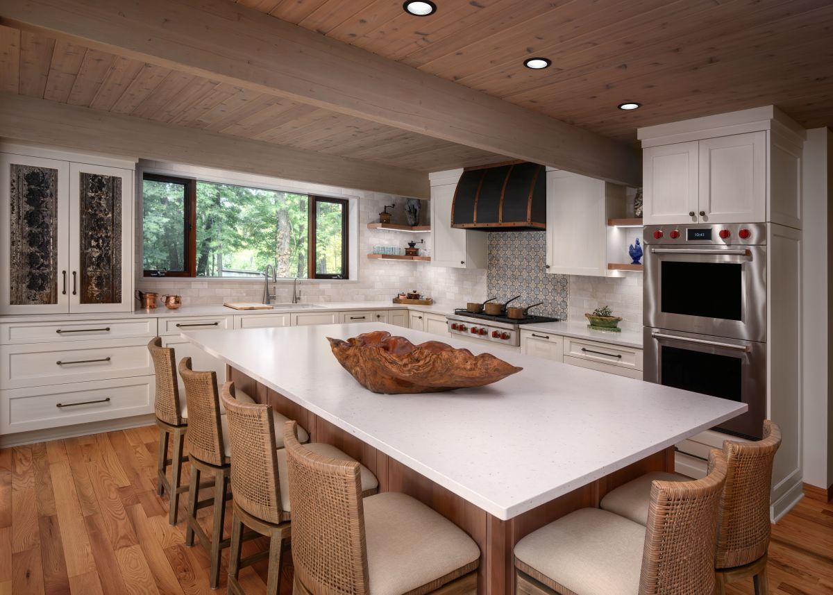 Bright modern kitchen with white island, wicker chairs, large window, and stainless steel appliances