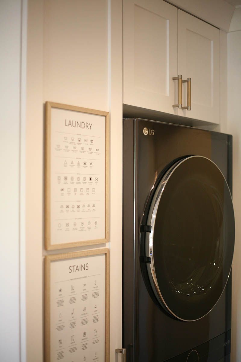 Kitchen cabinet with a large black front-loading washer or dryer and framed wall charts.