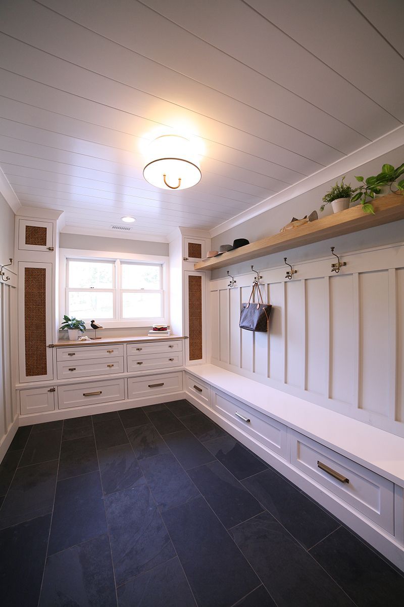 Bright white mudroom with built-in bench, coat hooks, cabinets, and dark slate floor