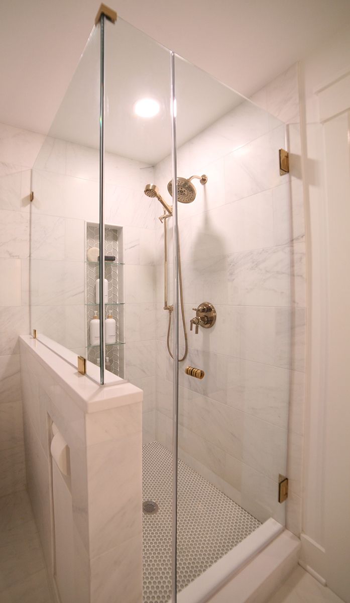 Glass-enclosed marble shower with handheld showerhead and chrome fixtures in a bright bathroom