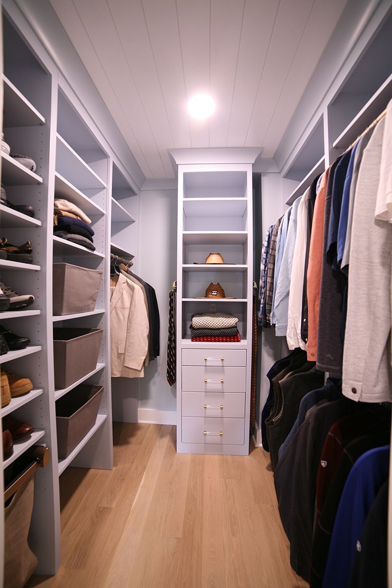 Walk-in closet with shelves, hanging clothes, drawers, and light wood flooring.