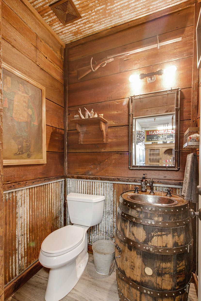 Rustic wood-paneled bathroom with toilet, barrel sink, mirror, and framed wall art.