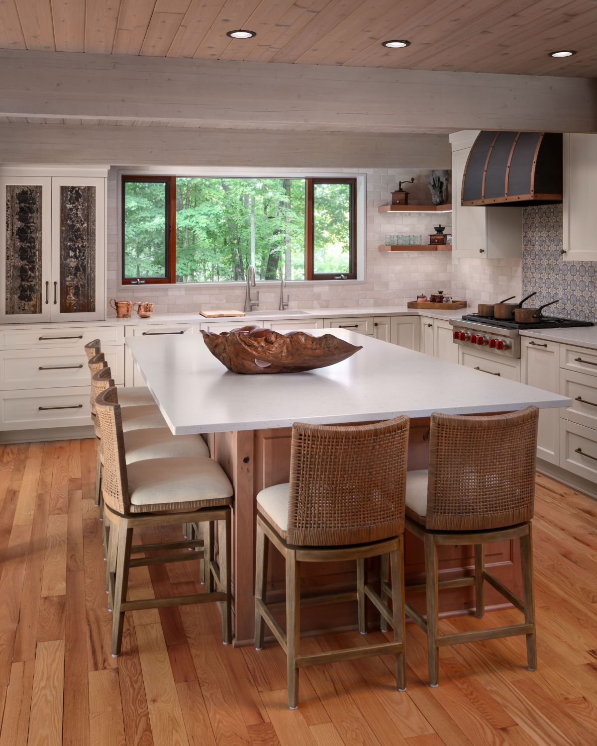 Modern kitchen with large white island, wicker stools, wood cabinets, and a window overlooking greenery