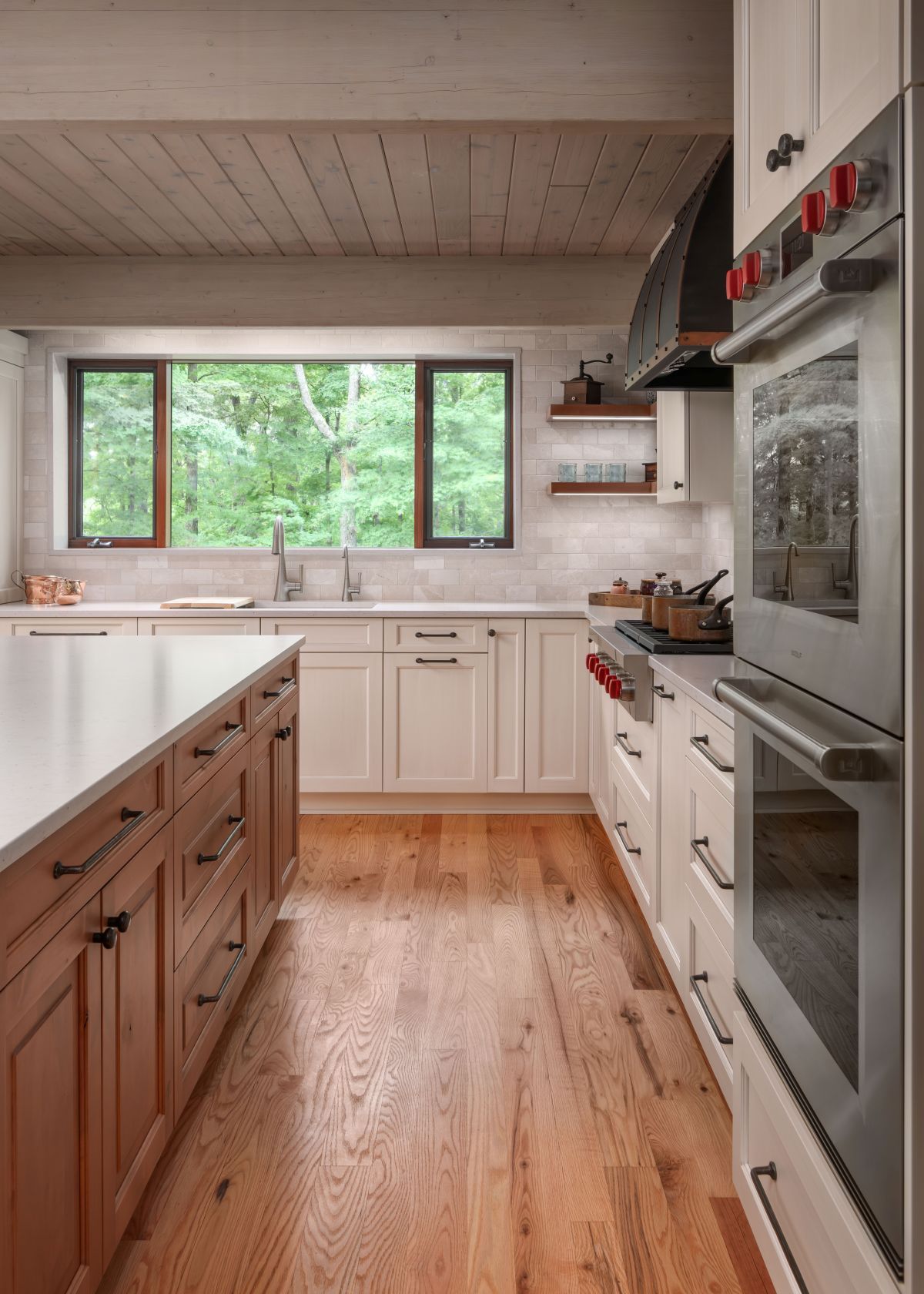 Modern kitchen with white cabinets, wood island, stainless oven, and a window overlooking greenery