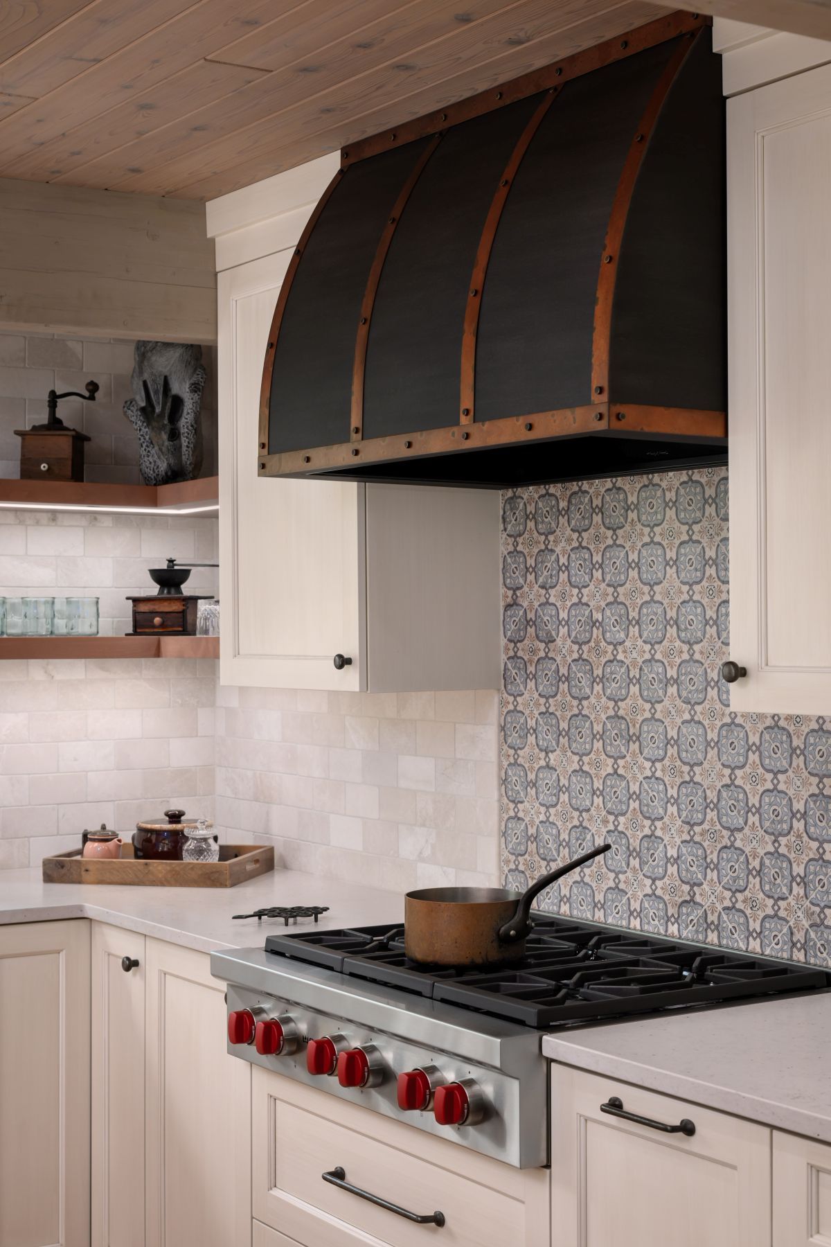 Cozy kitchen with white cabinets, patterned blue tile backsplash, and a stove with a saucepan under a dark hood