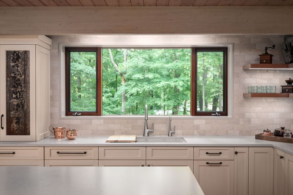Modern kitchen with beige cabinets, large window over sink, and green trees outside