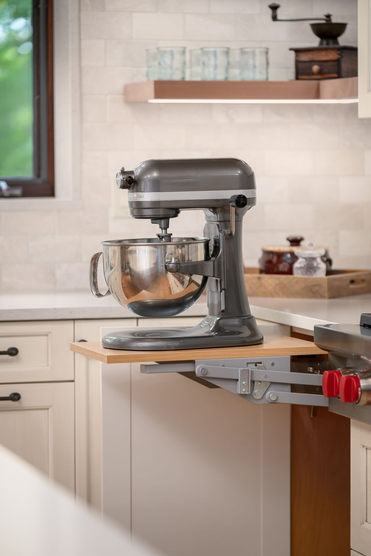 Silver stand mixer on a kitchen countertop next to a pull-out shelf in a bright modern kitchen