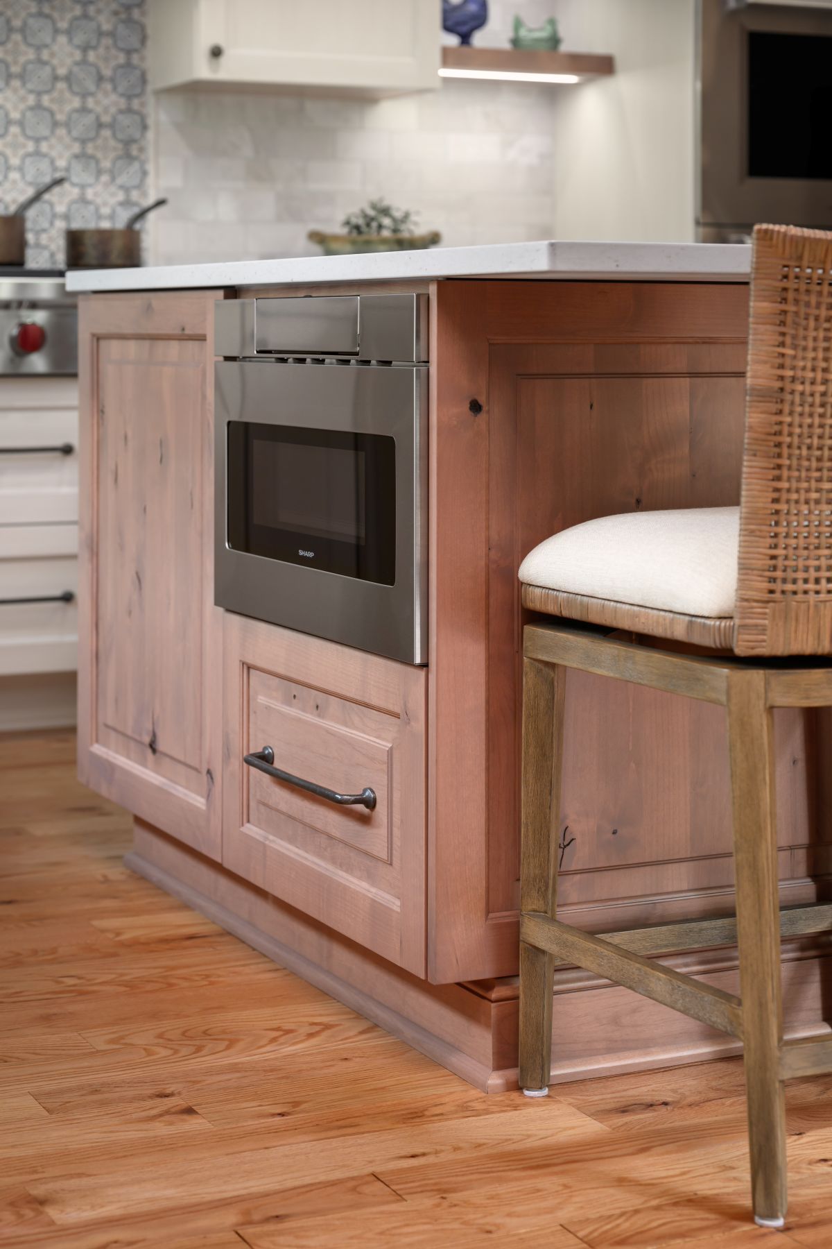 Kitchen island with built-in oven and wood cabinetry beside a wicker bar stool