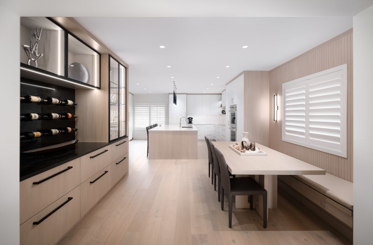 Bright modern kitchen with light wood cabinetry, white island, built-in wine fridge, and long dining bench.
