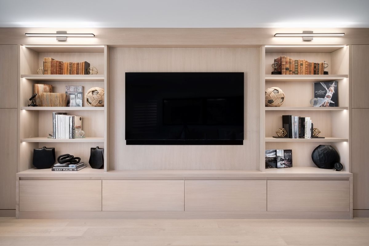 Built-in living room shelving with books, decor, and a large wall-mounted TV centered on a beige wall.