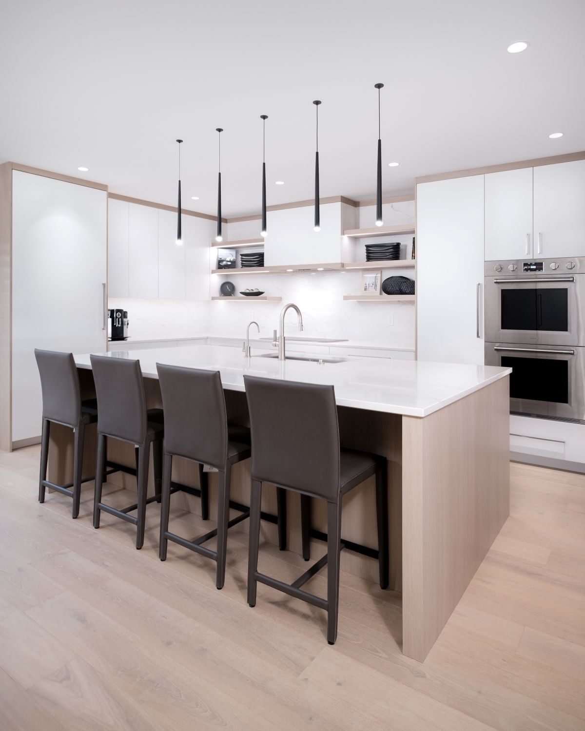 Modern white kitchen with island, barstools, built-in ovens, and pendant lights