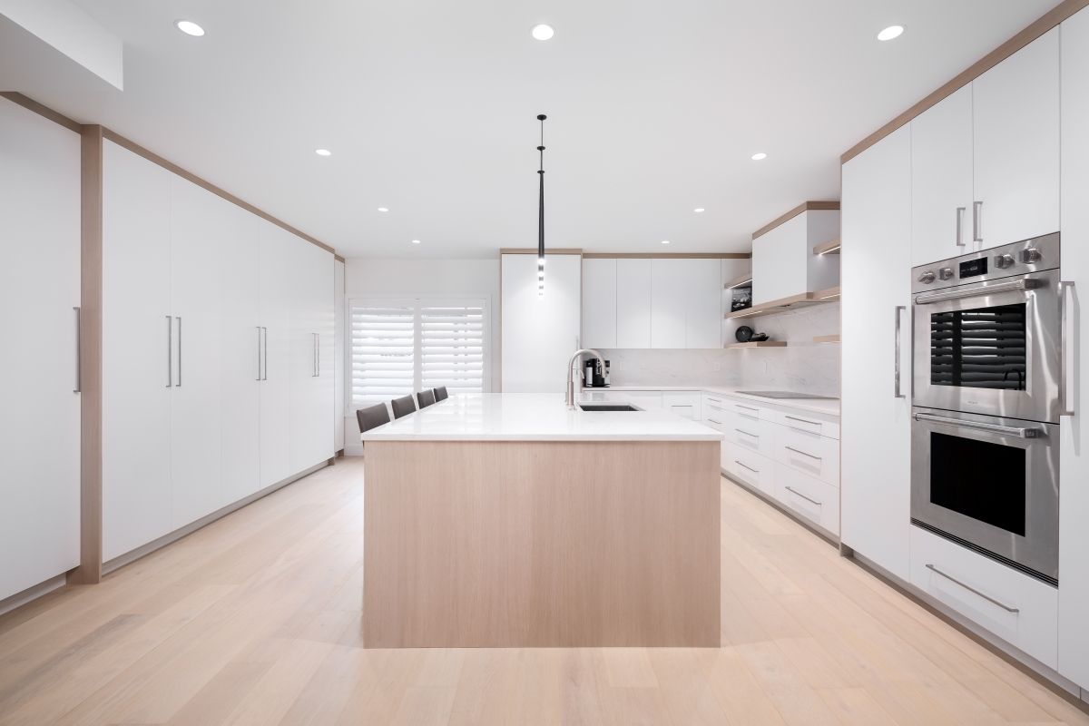 Bright modern white kitchen with island, built-in oven, and light wood floors