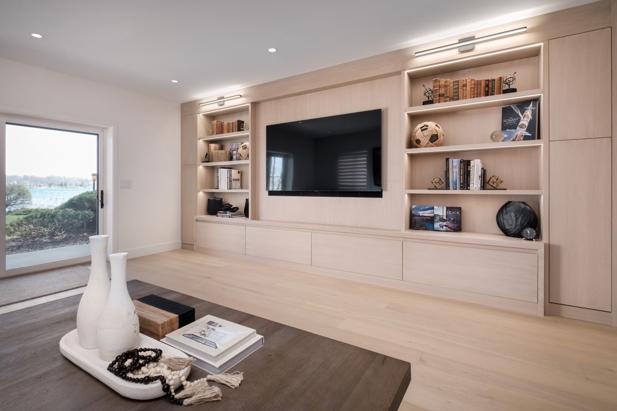 Modern living room with built-in shelves, large TV, and light wood finishes
