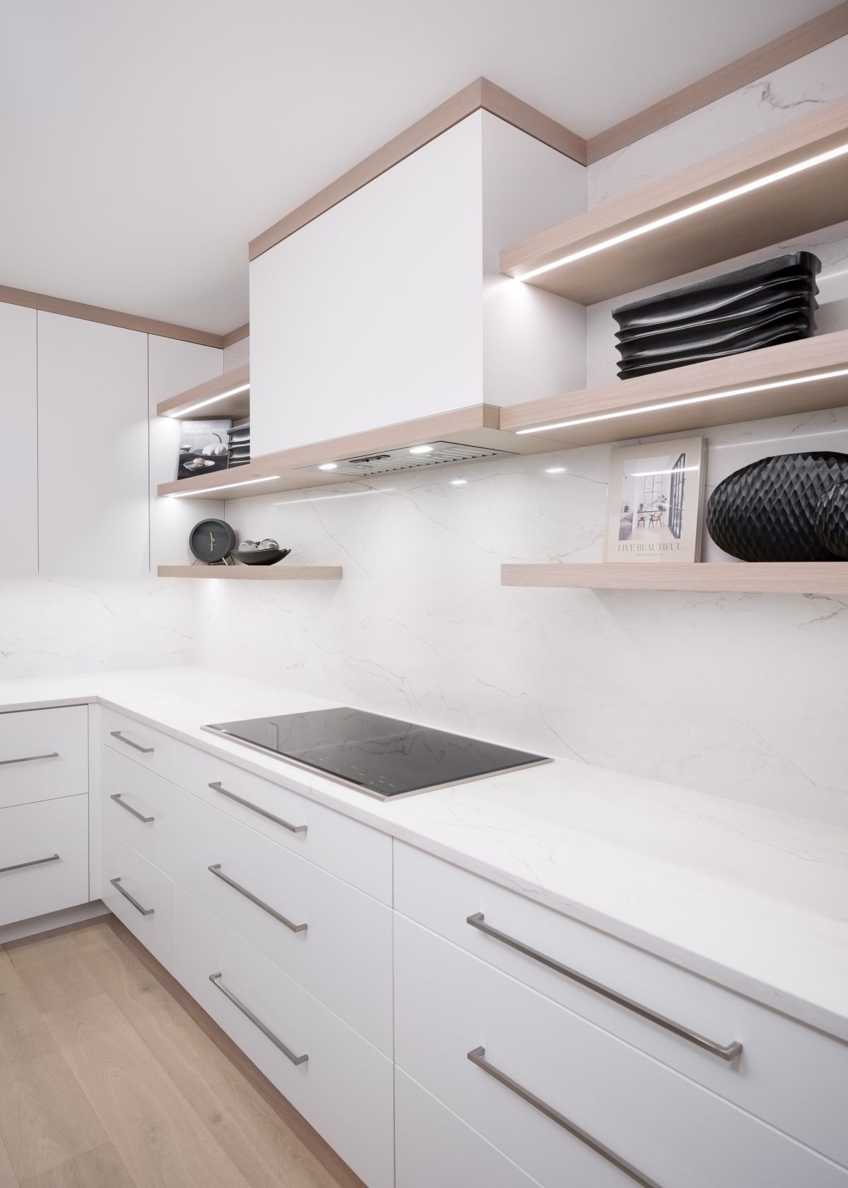 Modern white kitchen with sleek cabinets, countertop, built-in cooktop, and open shelves with neatly stacked items